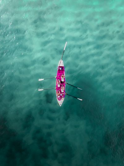 Aerial view of a pink rowing boat with four people on clear turquoise water, seen from directly above.